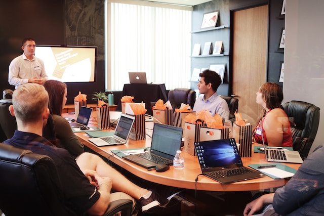 A meeting with people gathered around a boardroom table with laptops