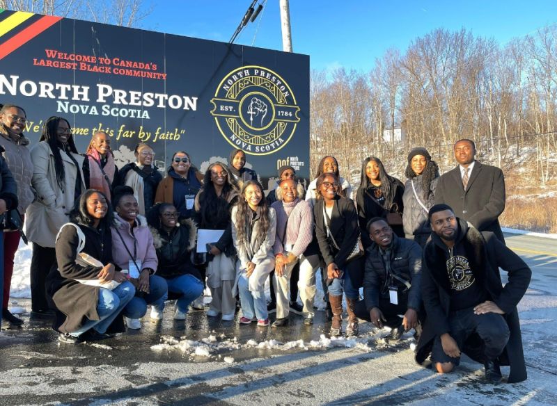 reBOOT alumni Brian Provo poses with a group of black law students in front of the sign for North Preston, NS.