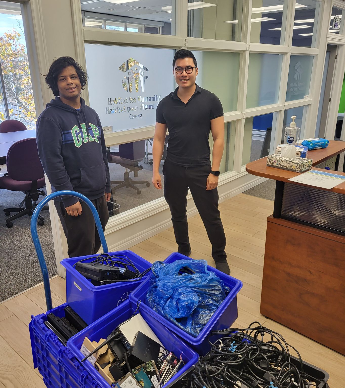reBOOT's Krish Saha (left) and Jameson from Habitat for Humanity GTA pose with bins full of equipment being donated by Habitat for Humanity GTA.