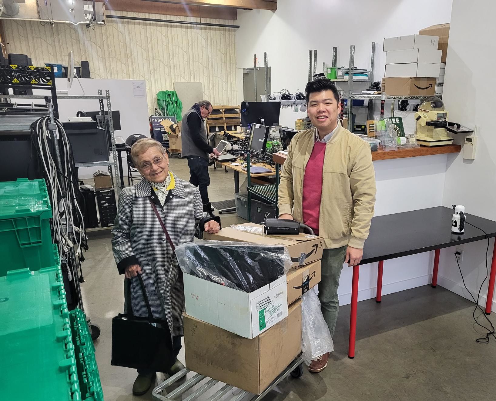 Steve Lee at the Vancouver reBOOT Canada office with Gladys from Lynn Valley and the pile of used equipment she gathered from neighbours for donation.